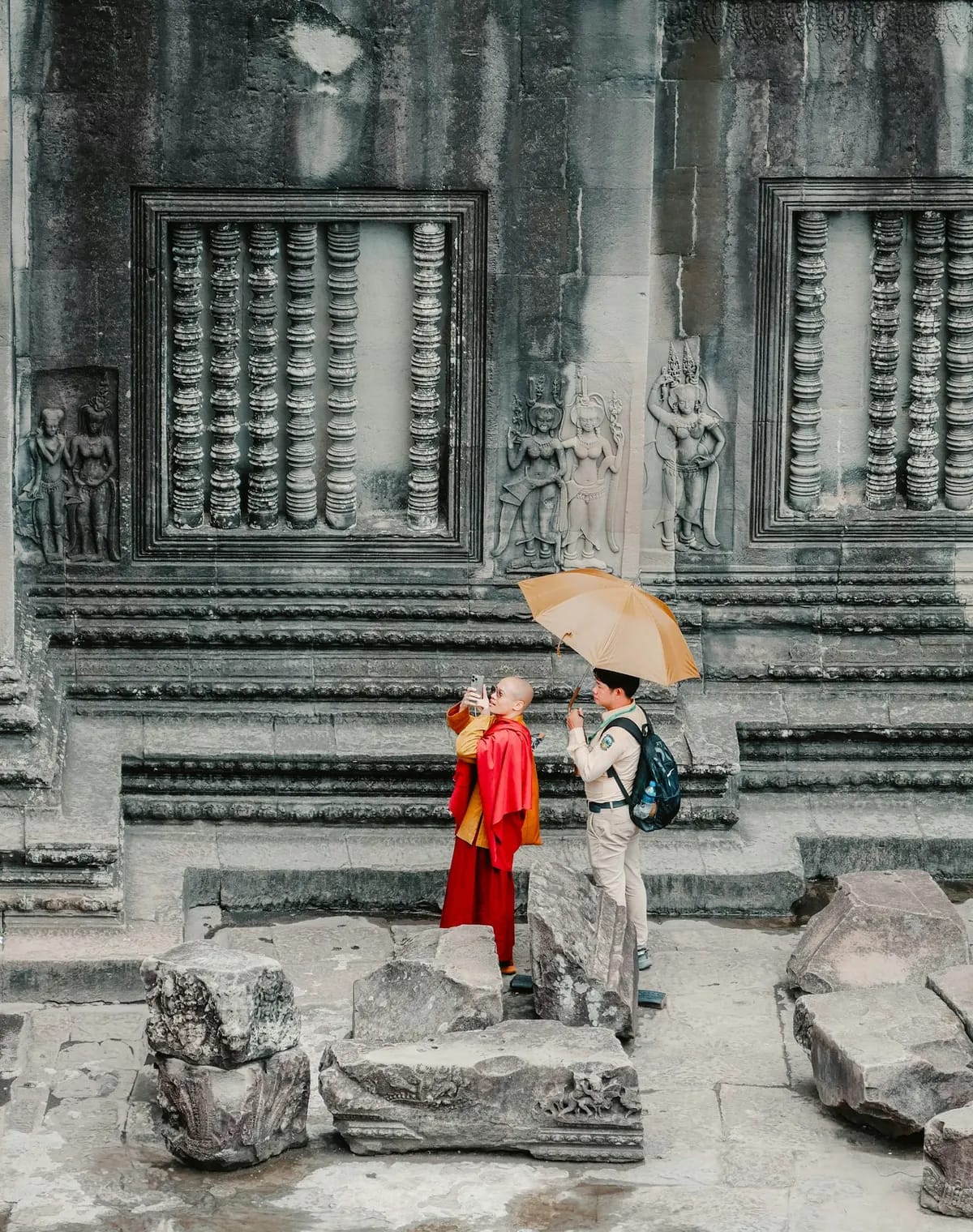 Two people under an umbrella by the carvings of Angkor Wat