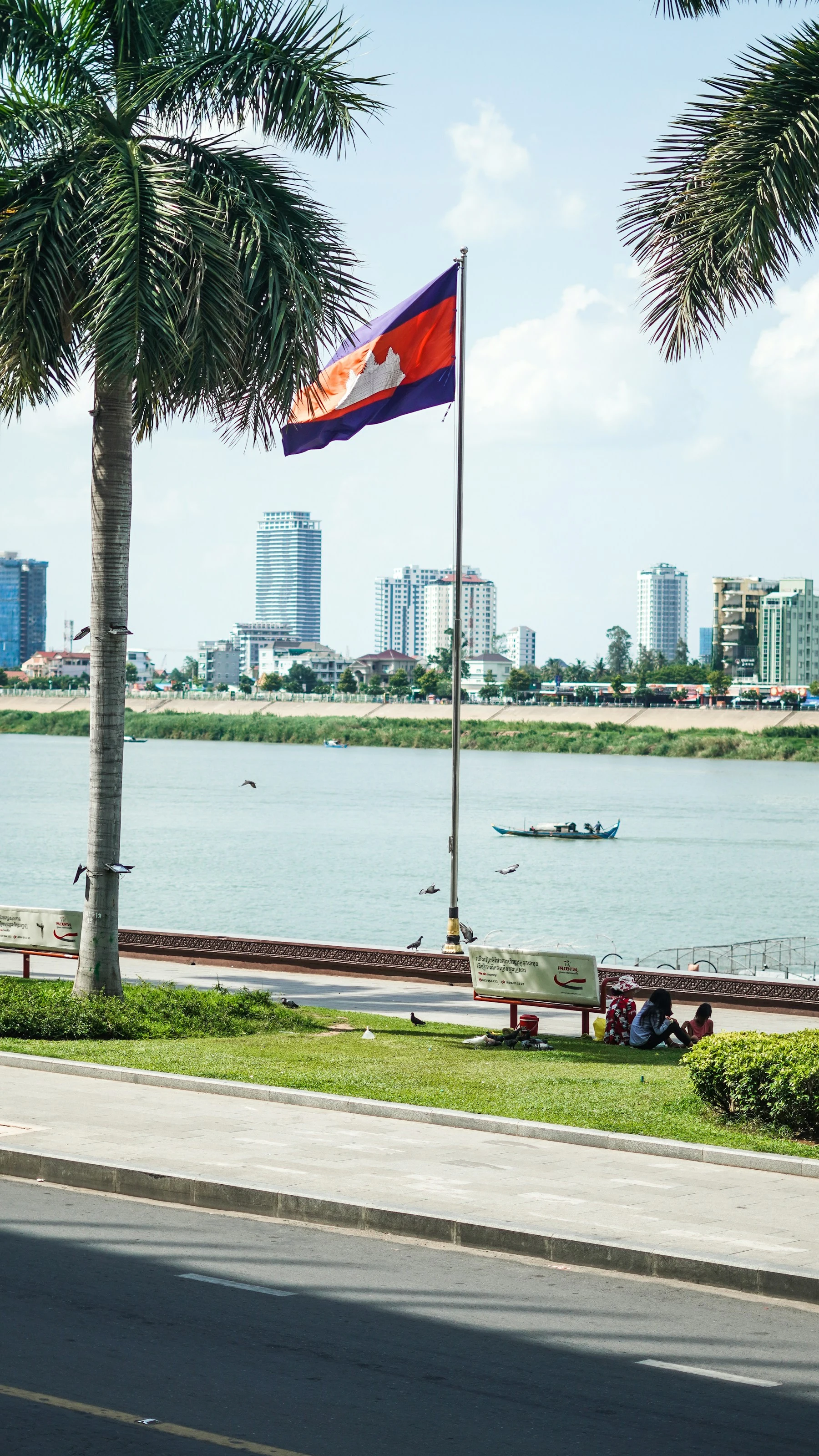 A Cambodian flag, palm trees and Phnom Penh’s riverfront.